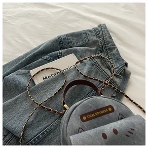 Detail of round light blue denim crossbody bag with cat facial features and leather strap