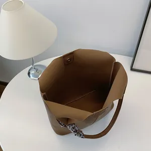 Brown pebbled leather tote bag with decorative scarf and magnetic closure on white table