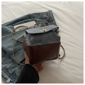 Detail of a denim and brown leather backpack with golden twist lock and chain strap