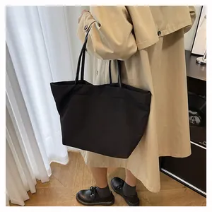 Bolso tote minimalista de lona negra con asas delgadas usado sobre una gabardina
