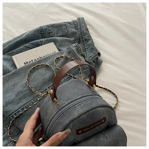 Detail of washed denim mini bag with brown leather handle and gold chain strap