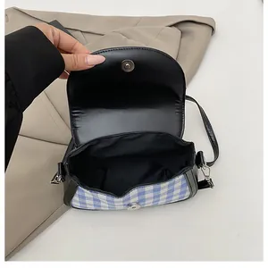 Detail of blue plaid fabric and magnetic clasp on a black leather crossbody handbag