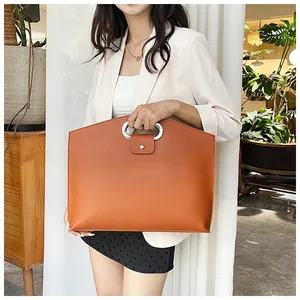 Detail of warm orange large capacity handbag featuring a unique oval metal cutout handle