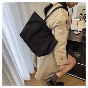 Detail of minimalist black canvas tote bag carried by a model in a modern urban setting