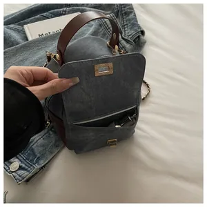 Detail of blue denim handbag featuring a front pocket with golden metallic twist lock
