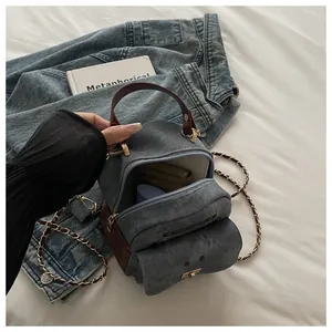 Detail of mini denim backpack with brown leather trim and golden chain strap
