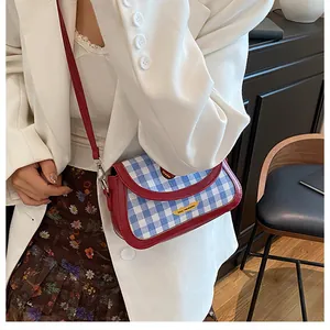 Detail of blue gingham crossbody bag with red leather trim on a white blazer outfit