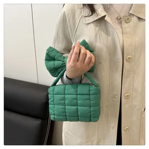 Detail of bright green quilted puffy handbag with oversized bow handle held by model