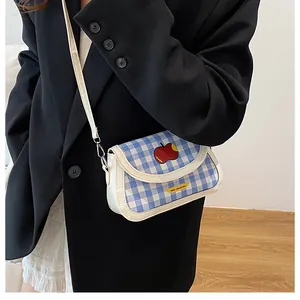 Detail showing blue plaid crossbody bag with red apple patch and white leather straps