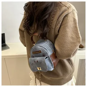 Close-up of mini denim cat backpack with brown leather trim and metal chain strap