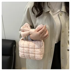 Detail of light pink quilted handbag featuring a large bow handle and soft fabric texture