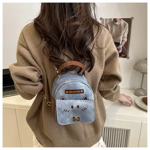 Detail of mini cat-themed denim backpack with chain strap on a model with yellow sweater
