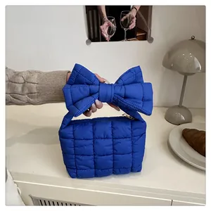 Detail of royal blue puffer bag featuring large bow handle and quilted texture