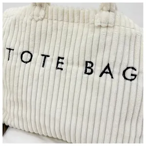 Détail d'un sac cabas en velours côtelé blanc avec texture nervurée et lettrage noir