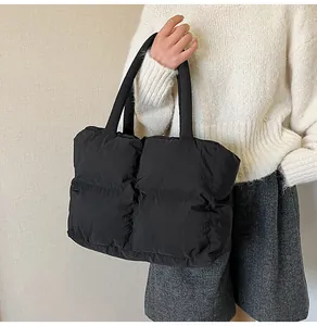 Detail of black quilted puffer tote bag with padded handles and glossy nylon texture