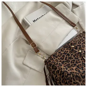 Detail of leopard print crossbody bag with brown leather strap and decorative fringe
