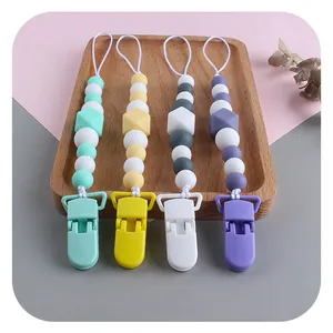 Silicone baby pacifier clips in pastel colors on a wooden tray with a minimalist background