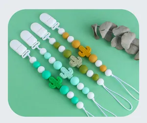 Détail de quatre attaches-tétines en silicone avec cactus sur fond vert clair