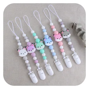Silicone pacifier clips with cat charms in multiple colors on a soft fabric background