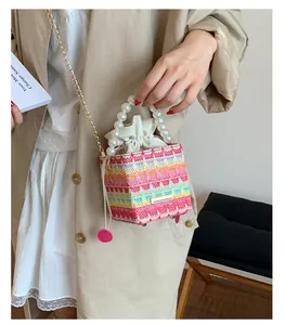 Détail d'un mini sac seau tissé avec poignée en perles et bandoulière en chaîne dorée chic