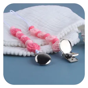 Pink silicone rose pacifier clip with metal fastener on soft blue and white background