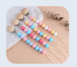 Detail of four silicone pacifier clips with wooden clamps and macaron beads