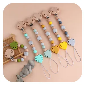 Beech wood and silicone leaf pacifier clips in various colors on a warm background