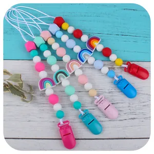 Silicone baby pacifier clips with rainbow design and soft beads on blue wood background