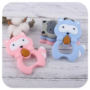 Cartoon raccoon silicone baby teether in pink, blue, and gray colors on white wood