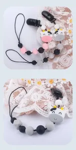 Detalle de los clips de silicona para chupete con cuentas de vaca sobre encaje blanco