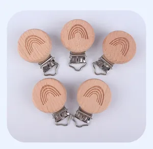 Dettaglio di cinque clip per succhietti in legno di faggio con motivi arcobaleno incisi