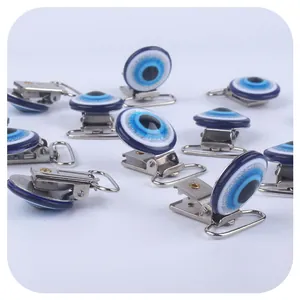 Silver metal pacifier clips with blue resin evil eye decoration in a flat lay view