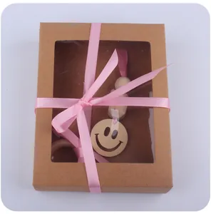 Détail d'un pendentif en bois smiley dans un coffret en kraft avec ruban rose