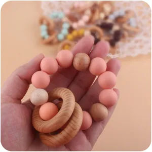 Pink silicone and natural wood baby teething ring rattle held in hand with soft warm background