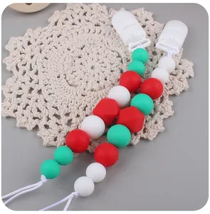 Detailed shot of Christmas silicone pacifier clips with red and green beads on a lace mat