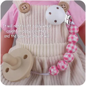 Close-up of pink checkered pacifier clip and silicone nipple attached to baby doll