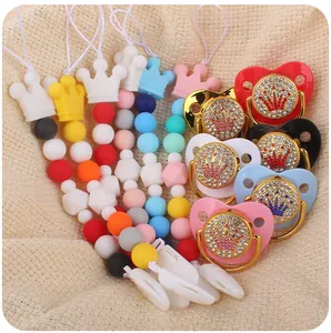 Detail of crown silicone pacifier clips with colorful beads on beige knit background