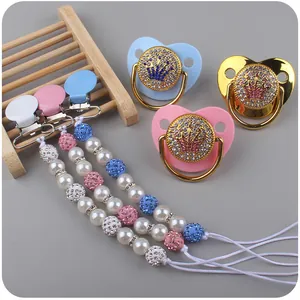 Detail view of baby pacifiers and pearl clips featuring rhinestone crown designs
