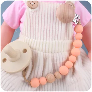 Chupete de silicona con clip de madera de haya y cuentas naranjas usado por una muñeca