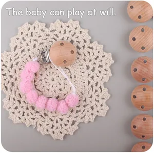 Detailed view of handmade pink pom-pom baby pacifier clip with natural wooden clasp