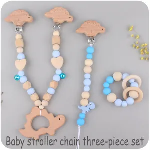 Close-up of blue silicone dinosaur stroller chain, pacifier clip and wooden teether set