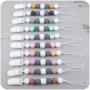 Flat lay set of 10 silicone baby pacifier clips in various Morandi colors with dry flowers