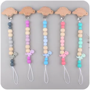 Five silicone and wood dinosaur baby pacifier clips in various pastel colors