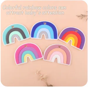 Detailed view of colorful silicone rainbow teething toys with heart cutouts on pink background