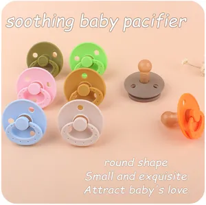 Flat lay of colorful round silicone pacifiers in multiple colors on a soft pink background