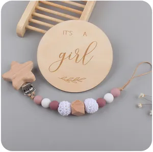 Detail of wooden milestone card and pink silicone pacifier clip for baby girls