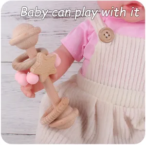 Detail of wooden baby rattle with pink silicone beads held by a doll on wood background