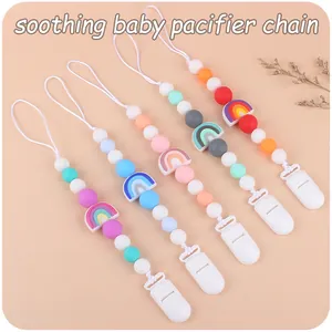 Flat lay of colorful silicone baby pacifier clips with rainbow charms in four pastel shades