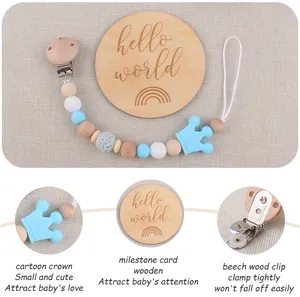 Detail of beech wood pacifier clip with blue silicone crown and 'hello world' milestone card