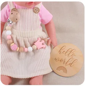 Close-up of pink silicone and beech wood baby pacifier clip set with hello world prop